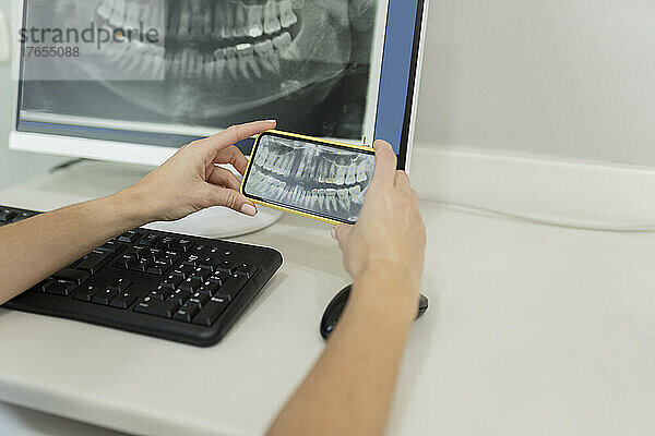 Zahnarzt untersucht Röntgenbild über Smartphone in Zahnklinik