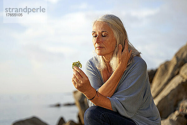 Frau mit grauem Haar hält Blume am Strand