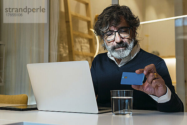 Leitender Freiberufler mit Kreditkarte und Laptop zu Hause