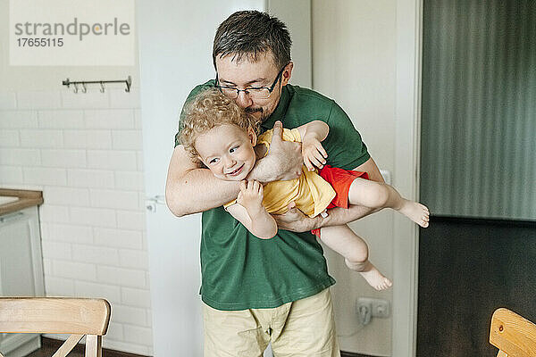 Playful man carrying daughter and kissing on head in kitchen