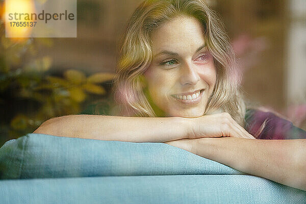 Schöne lächelnde Frau mit blonden Haaren  die zu Hause auf dem Sofa lehnt