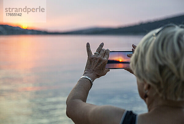 Ältere Frau fotografiert im Urlaub den Sonnenuntergang per Smartphone