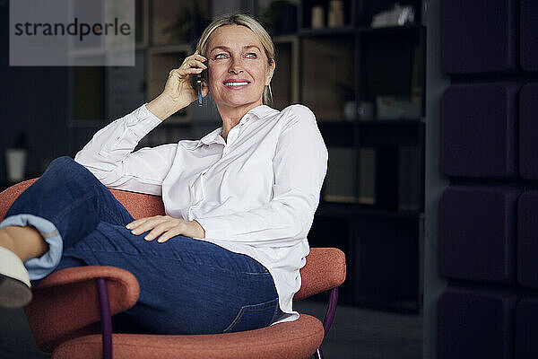 Lächelnde Geschäftsfrau  die im Büro mit dem Mobiltelefon spricht