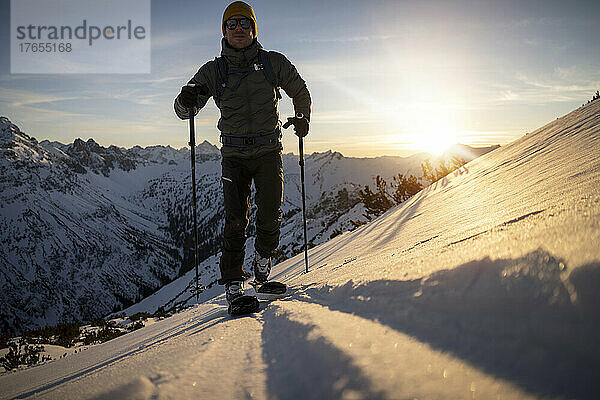 Mann mit Skistock läuft bei Sonnenaufgang auf schneebedecktem Berg