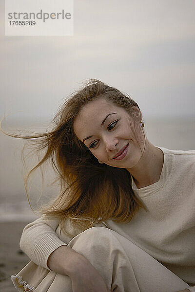 Schöne Frau mit langen Haaren sitzt bei Sonnenuntergang am Strand
