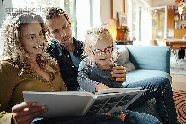 Vater und Mutter schauen sich die süße Tochter an  die im Wohnzimmer zu Hause ein Buch liest