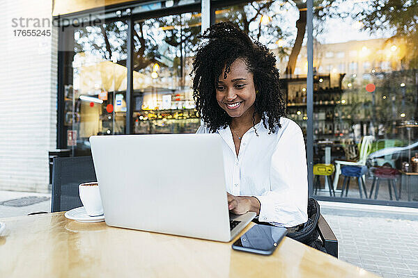 Glückliche Geschäftsfrau sitzt mit Laptop im Straßencafé
