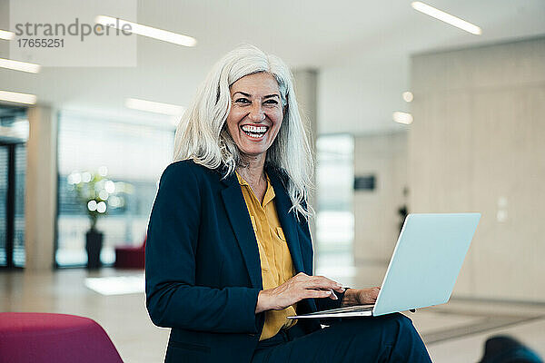 Laughing businesswoman with laptop sitting in office