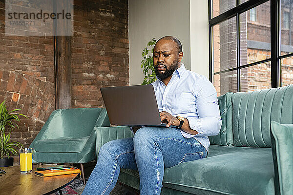 Geschäftsmann sitzt auf Sofa und benutzt Laptop im Büro