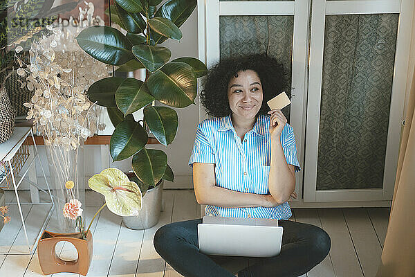 Nachdenkliche Frau mit Kreditkarte und Laptop beim Online-Einkauf zu Hause