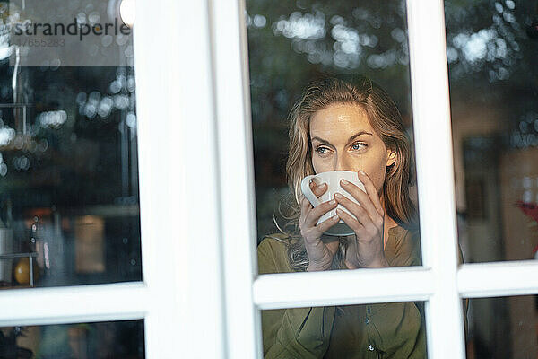 Blonde Frau trinkt Kaffee  gesehen durch Glasfenster