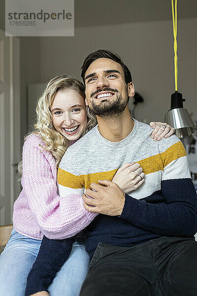 Lächelndes junges Paar sitzt zusammen zu Hause