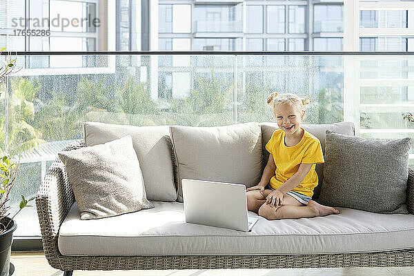Glückliches Mädchen mit Laptop  das zu Hause auf dem Sofa sitzt