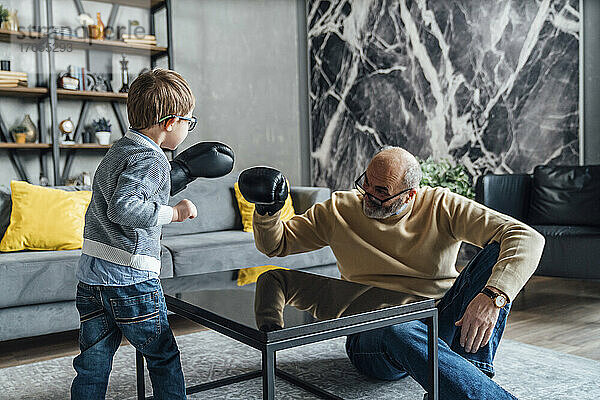 Verspielter Großvater und Enkel mit Boxhandschuh spielen im heimischen Wohnzimmer