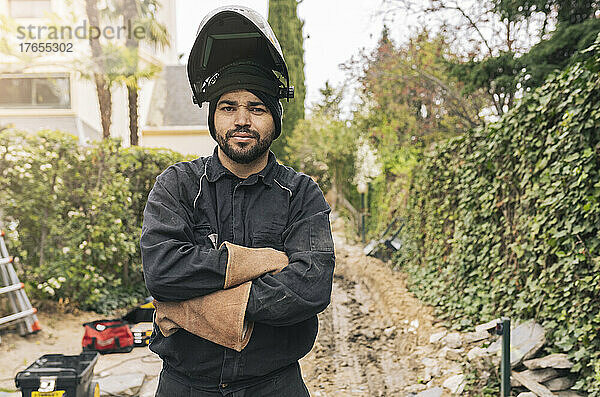 Schweißer mit Schweißhelm steht mit verschränkten Armen auf der Baustelle