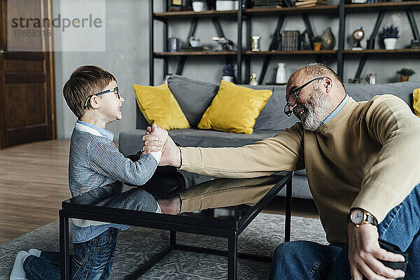 Glücklicher älterer Mann beim Armdrücken mit Enkel im heimischen Wohnzimmer