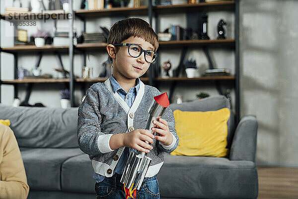 Netter Junge mit Brille und Spielzeugrakete zu Hause