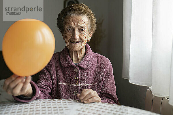 Smiling woman with orange balloon sitting at dining table