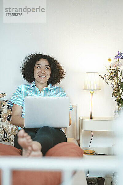 Lächelnde Frau mit Laptop sitzt zu Hause im Bett