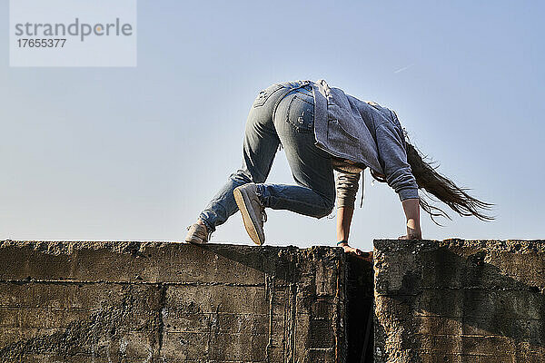 Junge Frau springt über Betonmauer  Rückansicht