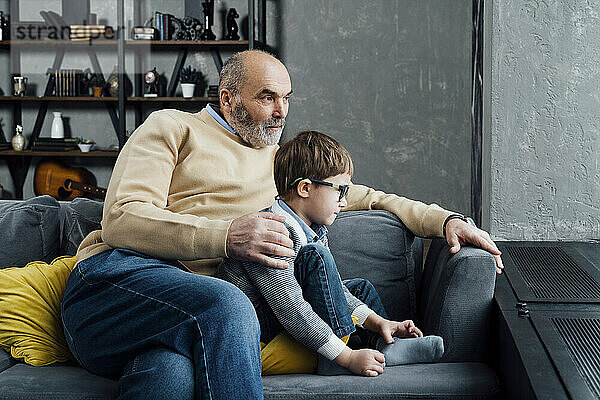 Älterer Mann mit Enkel sitzt zu Hause auf dem Sofa im Wohnzimmer