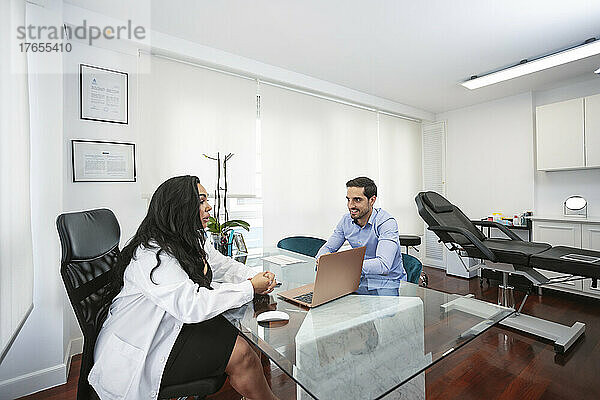 Dermatologe diskutiert mit dem Patienten  der am Schreibtisch in der ästhetischen Klinik sitzt