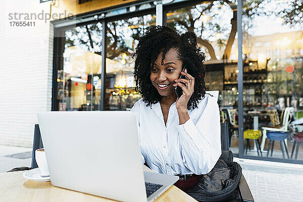 Glückliche Geschäftsfrau mit Laptop und Handy im Straßencafé
