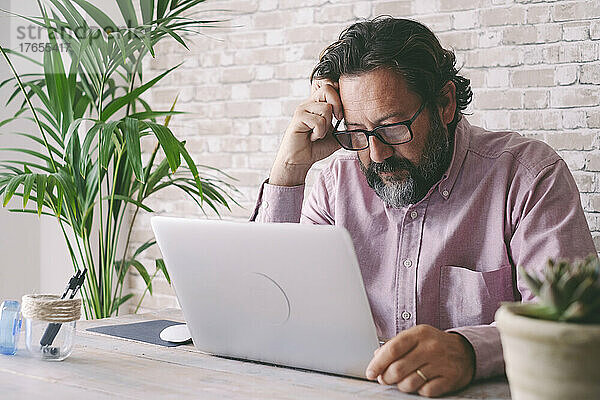 Trauriger Geschäftsmann mit Laptop am Tisch sitzend