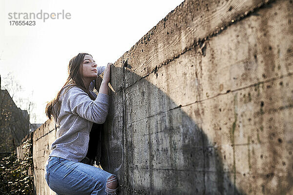 Neugierige junge Frau blickt über Betonmauer