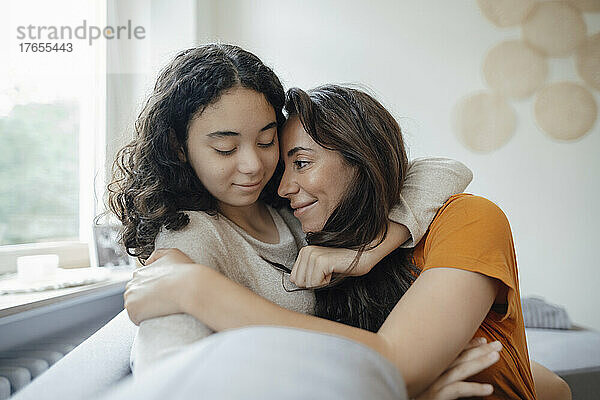 Teenager-Mädchen umarmt Mutter  die zu Hause auf dem Sofa sitzt
