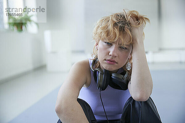 Young woman wearing headphones sitting with hand in hair