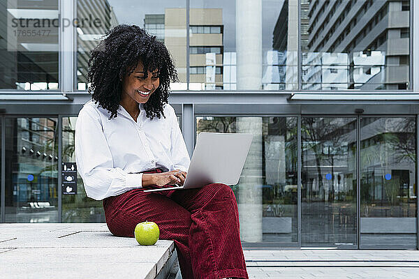 Lächelnde Geschäftsfrau mit Laptop sitzt im Büropark