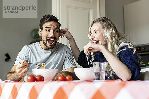 Verspieltes Paar isst zu Hause am Esstisch