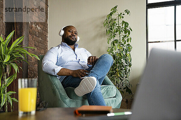 Geschäftsmann hört Musik über drahtlose Kopfhörer  sitzt auf einem Sessel im Büro