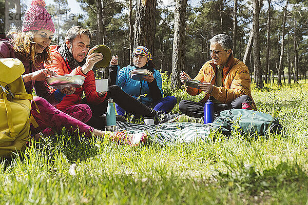 Lächelnde Männer und Frauen essen an sonnigen Tagen im Wald Essen
