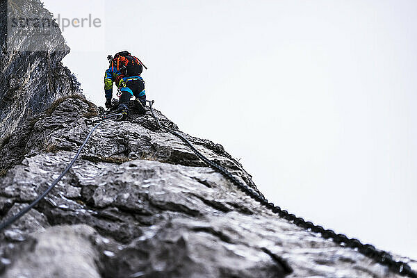 Mann klettert auf felsigen Berg über Klettersteig