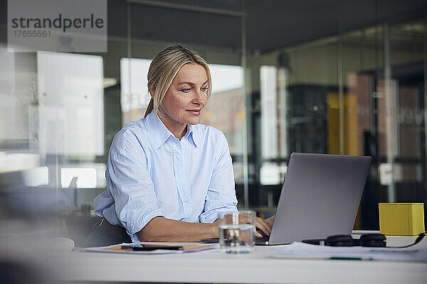Lächelnde Geschäftsfrau benutzt Laptop am Schreibtisch im Büro