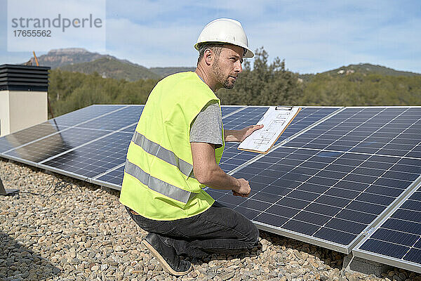 Ingenieur mit Blaupause vor Sonnenkollektoren an einem sonnigen Tag