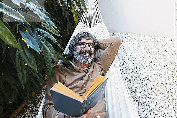 Glücklicher Mann mit Buch entspannt in der Hängematte im Hinterhof