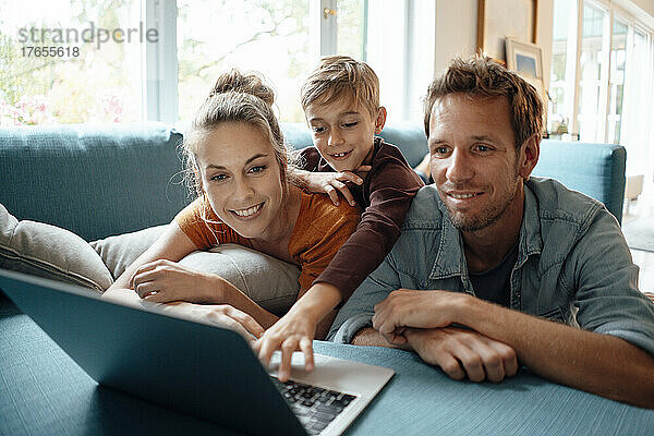 Glückliche Familie  die zu Hause einen Laptop auf dem Sofa teilt