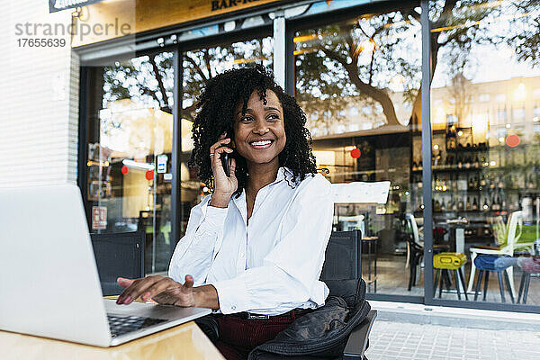 Lächelnde Geschäftsfrau mit Laptop und Smartphone im Straßencafé