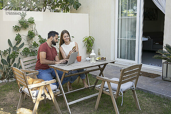 Glückliche Frau teilt Smartphone mit Mann  der im Hinterhof sitzt