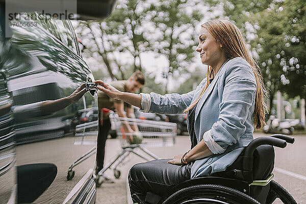 Lächelnde junge Frau sitzt im Rollstuhl und öffnet die Autotür