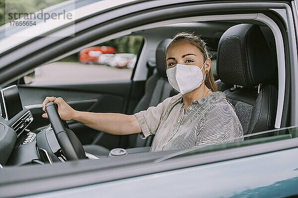 Junge Frau mit schützender Gesichtsmaske fährt Auto
