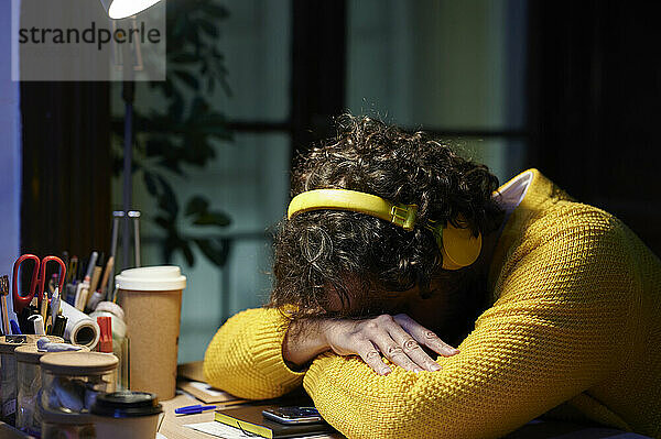 Businessman resting head on desk listening music through headphones at office