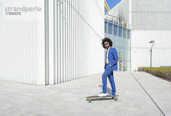 Geschäftsmann mit Skateboard steht an einem sonnigen Tag Hand in der Tasche