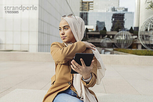 Geschäftsfrau mit Hijab sitzt mit Tablet-PC im Büropark