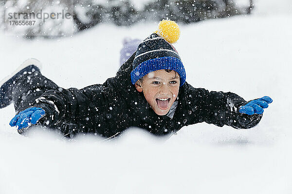 Verspielter Junge streckt die Zunge heraus und liegt auf Schnee
