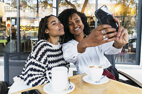 Lächelnde Kollegen  die im Straßencafé ein Selfie mit dem Smartphone machen