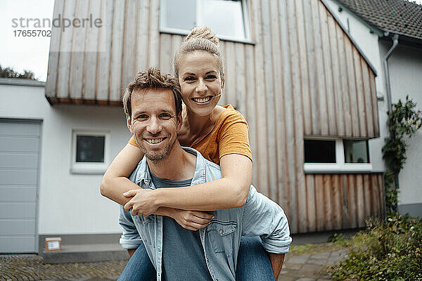 Glücklicher Mann gibt seiner blonden Freundin Huckepackfahrt im Hinterhof